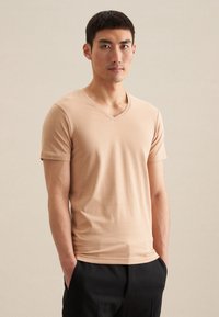 T-shirt beige à col en V en tissu doux, à manches courtes, au design ajusté avec une texture lisse. Porté avec un pantalon noir.