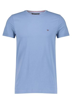 Vaaleansininen lyhythihainen t-paita, joissa pyöreä pääntie ja pieni Tommy Hilfiger -lippulogo vasemmalla rinnalla sekä brändätty kauluksen sisäpuolen yksityiskohta.