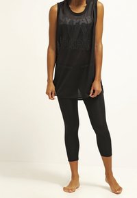 Czarna siateczkowa koszulka na ramiączkach z logo "IVY PARK", w połączeniu z czarnymi legginsami. Oba elementy mają dopasowany krój idealny do aktywności fizycznej.