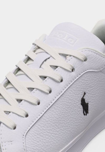 Άσπρο δερμάτινο αθλητικό παπούτσι με εκρού κορδόνια, με το μαύρο λογότυπο Polo ενός παίκτη πόλο πάνω σε άλογο στην πλευρική επιφάνεια.