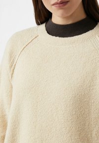 Beżowy sweter o fakturowanej powierzchni z okrągłym dekoltem, z ciemnobrązowym, prążkowanym kołnierzem i rękawami raglanowymi. Miły i przytulny wygląd.