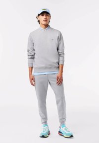 Set di maglione grigio e pantaloni della tuta con una camicia azzurra sottostante. Un cappellino blu e sneakers colorate completano l'outfit. Tessuto morbido, vestibilità rilassata.