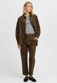 Brown corduroy shirt and matching pants, grey t-shirt underneath, black slip-on shoes, relaxed fit with rolled cuffs, button detail on pants.