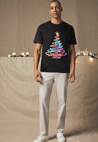 Sort kortærmet t-shirt med et farverigt, svunget lys-træ grafik med en stjerne. Sættes sammen med lyse beige bukser og hvide sneakers.