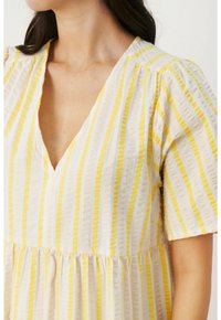 Biała sukienka z pionowymi żółtymi paskami, dekoltem w kształcie litery V, bufiastymi rękawami i marszczoną talią. Materiał wydaje się lekki i miękki.