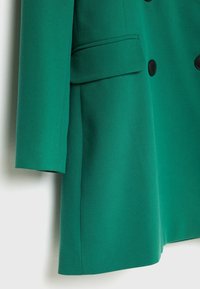 Abrigo verde de doble botonadura hecho de un tejido texturizado, con botones negros, un bolsillo en el pecho y una silueta entallada.