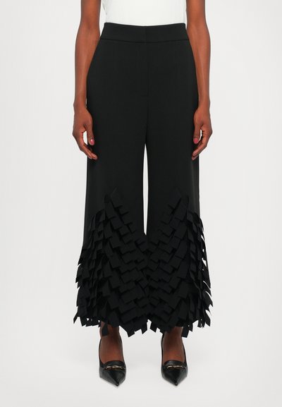 Pantaloni neri con un design a gamba larga, caratterizzati da una texture a strati con volant all'orlo. Materiale liscio e vita aderente.
