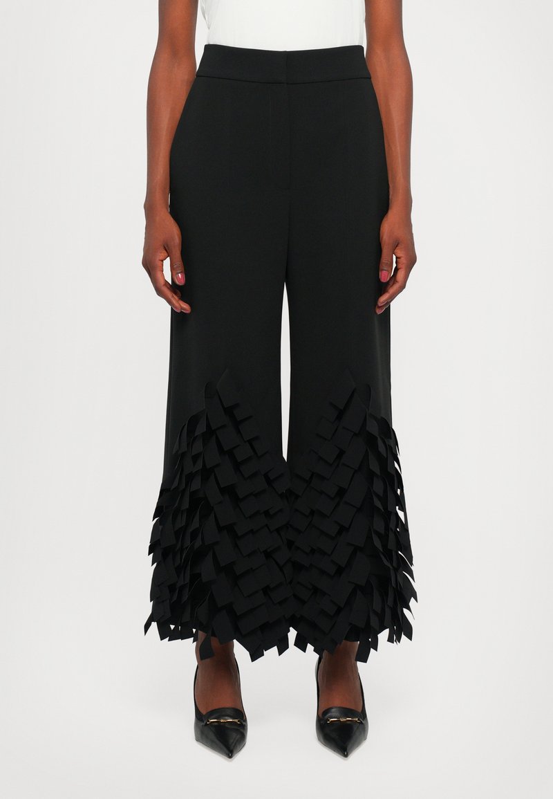 Pantalones negros con un diseño de pierna ancha, que presentan una textura de volantes en capas en el dobladillo. Material suave y cintura ajustada.