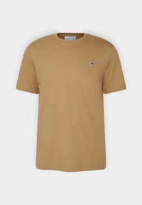 Brązowa bawełniana koszulka z okrągłym dekoltem, krótkimi rękawami i małym zielonym logo Lacoste na lewej piersi. Gładka tekstura.