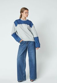Gray and blue color-blocked oversized sweatshirt with long sleeves, paired with wide-leg denim jeans, featuring frayed hems and a relaxed fit.