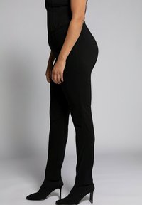 Pantaloni neri aderenti con una texture liscia, caratterizzati da una vita alta e linee di cucitura pulite, abbinati a scarpe nere con tacco alto.
