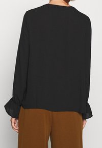 Blouse noire à manches longues avec une coupe décontractée. Présente des manches bouffantes transparentes et un ourlet arrondi. Fabriquée en tissu léger et lisse.