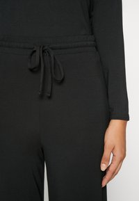 Zwarte jogger-stijl broek gemaakt van zachte stof, met een elastische tailleband met trekkoord en een ontspannen pasvorm.
