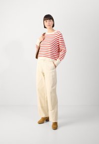 Röd och vit randig stickad tröja med en krämfärgad krage, tillsammans med beige vida byxor och bruna klackboots med blockklack.