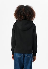Sweatshirt preto com capuz, feito de tecido macio, apresentando um bolso canguru e punhos canelados, combinado com uns jeans azuis de corte largo.