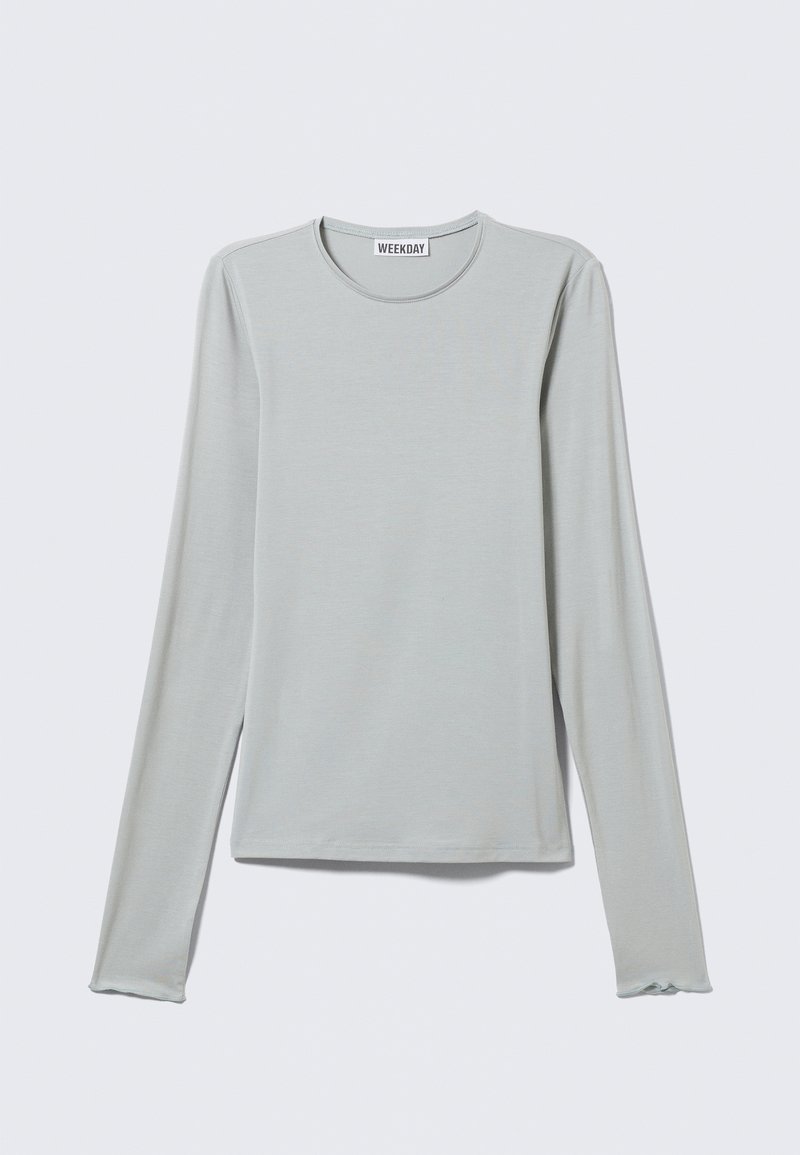 Camiseta de manga larga gris claro confeccionada en tela suave, con escote redondo y puños sutilmente ondulados. Diseño minimalista sin estampados.