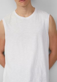 Witte mouwloze shirt met een ronde halslijn en subtiele textuur. Heeft een klein "QS" logo geborduurd aan de voorkant.
