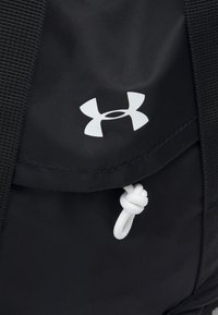 Czarny plecak z tkaniny z białym logo Under Armour, z zamknięciem na sznurek z węzłem oraz teksturowanym materiałem.
