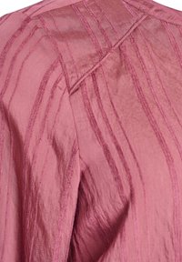 Ružová látka s vertikálnymi zvýšenými pruhmi a viditeľným stehom, zobrazená v blízkom zábere s textúrou a záhybmi.