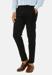Pantaloni neri con vestibilità slim, realizzati in tessuto liscio, dotati di tasche laterali e vita piatta, abbinati a mocassini marroni.