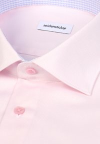 Chemise habillée pour hommes de couleur rose clair avec col à pointes écartées et deux boutons roses visibles, affichant l'étiquette "seidensticker" à l'intérieur du col.