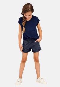 Navy blue short-sleeve t-shirt with a relaxed fit, paired with grey shorts featuring an elastic waistband and drawstring. White sneakers.