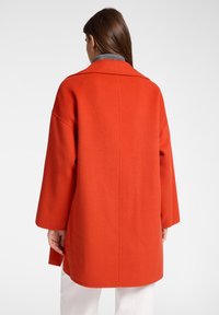 Cappotto rosso in misto lana con vestibilità comoda, maniche larghe e dettaglio con cucitura posteriore. Presenta un colletto con revers e arriva a metà coscia.