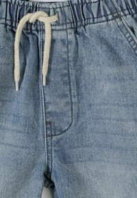 Pantalon en denim bleu clair avec taille élastique et cordon tressé blanc noué à l'avant.