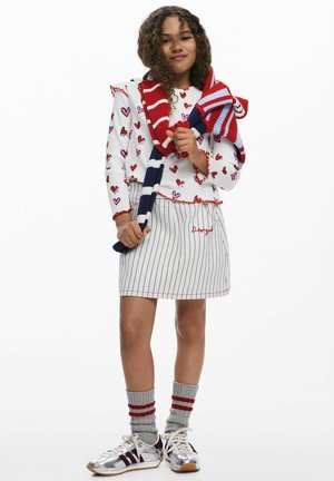 Maglietta bianca a maniche lunghe con motivi a cuore rossi e rosa, gonna a righe bianche e blu navy, sciarpa a righe rosse e blu, sneakers argento, calzini grigi.