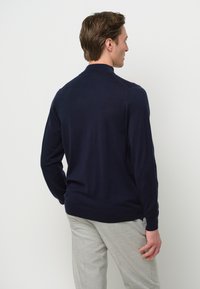 Dunkelblauer Strickpullover mit langen Ärmeln und geripptem Saum. Verfügt über einen klassischen Kragen und eine glatte Textur, getragen über hellgrauen Hosen.