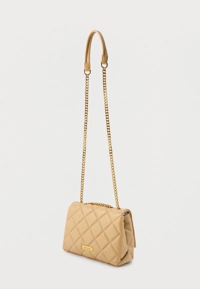 Μπεζ τσάντα ώμου από δερματίνη με επένδυση σε σχέδιο καπιτονέ, με λουρί αλυσίδα σε χρυσό χρώμα και ορθογώνια μεταλλική πινακίδα με λογότυπο στο μπροστινό μέρος.