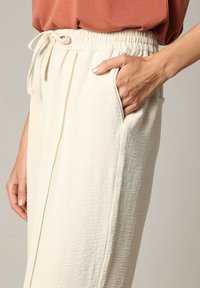 Lichtbeige, gestructureerde broek met een elastische tailleband en trekkoord. Voorzien van zijzakken en een recht gesneden ontwerp.