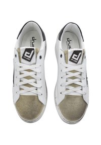 White sneakers with black accents and beige suede toe. Features flat laces, round toe, and logo patch on tongue. Smooth material finish.