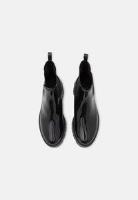 Une paire de bottes Chelsea noires brillantes avec des côtés élastiques et des tirettes, vues de dessus sur un fond blanc.