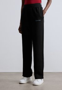 Czarne spodnie dresowe o luźnym kroju, z elastycznym pasem, kieszeniami po bokach oraz małym haftowanym logo na lewej nogawce.