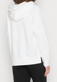 Sudadera blanca con capucha y corte relajado, que presenta aberturas laterales y puños acanalados, fabricada con una tela suave y cómoda.