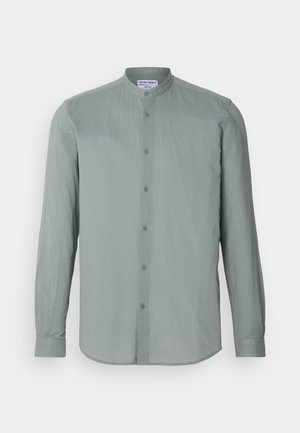 Camisa de manga longa, com botões, na cor verde claro, feita de um tecido texturizado. Possui colarinho em banda e linhas verticais subtis.