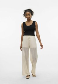 Top sin mangas negro con textura acanalada y bordes ondulados, combinado con pantalones sueltos de rayas crémos que son transparentes y cuentan con cintura elástica.