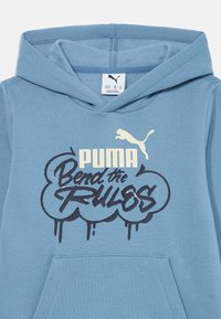 Blå hoodie i mjuk bomull med en känguruficka. Har grafiken "PUMA" och "Bend the Rules" i svart och krämfärgad. Huva design.
