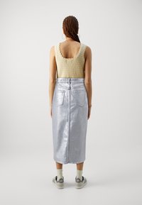 Bej kötött tank top fodros szegéllyel, ezüst metál midi szoknyával párosítva, hátul zsebekkel és cipzáras záródással.
