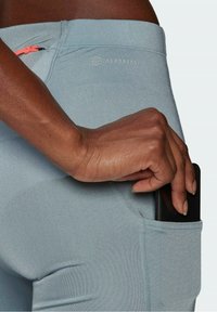 Jasnoniebieskie legginsy sportowe o dopasowanym kroju z boczną kieszenią. Materiał jest gładki i elastyczny, z logo blisko pasa.