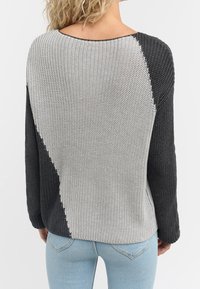 Pull en tricot avec un design en blocs de couleurs comprenant des sections grises et noires, encolure ronde et manches longues. Tissu texturé, coupe ample.