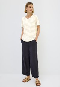 V-udskæring, kortærmet, crème-stribet t-shirt kombineret med mørke, løse linnedbukser og lysebrune sandaler med spænde detalje.