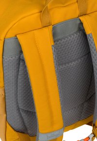 Zaino giallo con spallacci in rete grigia imbottiti e corpo in tessuto resistente; include hardware arancione e dettagli di texture sottili.