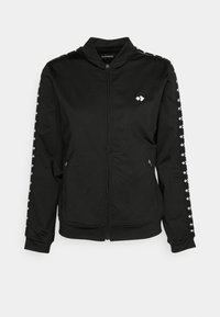 Veste noire zippée avec des motifs losanges blancs sur les manches et la poitrine, poches latérales zippées et col montant.