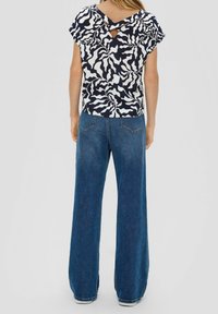 Haut à manches courtes à motif bleu marine et blanc avec un dos découpé, associé à un jean en denim bleu taille haute à jambes larges.