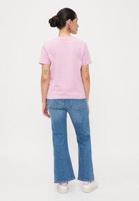Rosa kortermet t-skjorte i bomull, med rett passform. Kombinert med lyseblå bustete jeans og hvite joggesko med rosa detaljer.