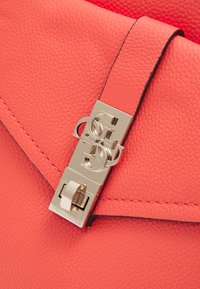 Borsa a mano in pelle corallo con superficie testurizzata. Presenta una chiusura in tonalità oro con design del logo intrecciato e cuciture a contrasto.
