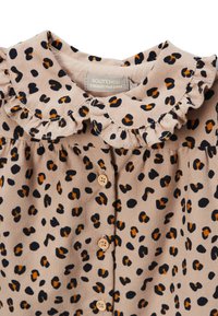 Robe en imprimé léopard en tissu beige doux. Présente un col volé et des boutons en bois. Motif à pois dans des teintes de noir et d'orange.