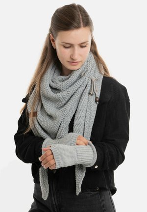 Lichtgrijze gebreide sjaal draped om de nek met bijpassende vingerloze handschoenen. De sjaal heeft een gestructureerd patroon en een houten accent.